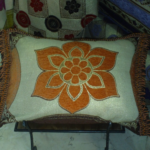 Housse de coussin marocaine jaune orangé ornée de motifs en fleur et cernée d'un liseré.